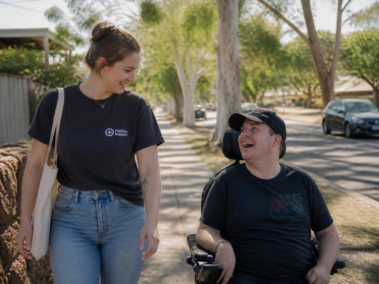 A support worker walking and talking with a participant using a power wheelchair